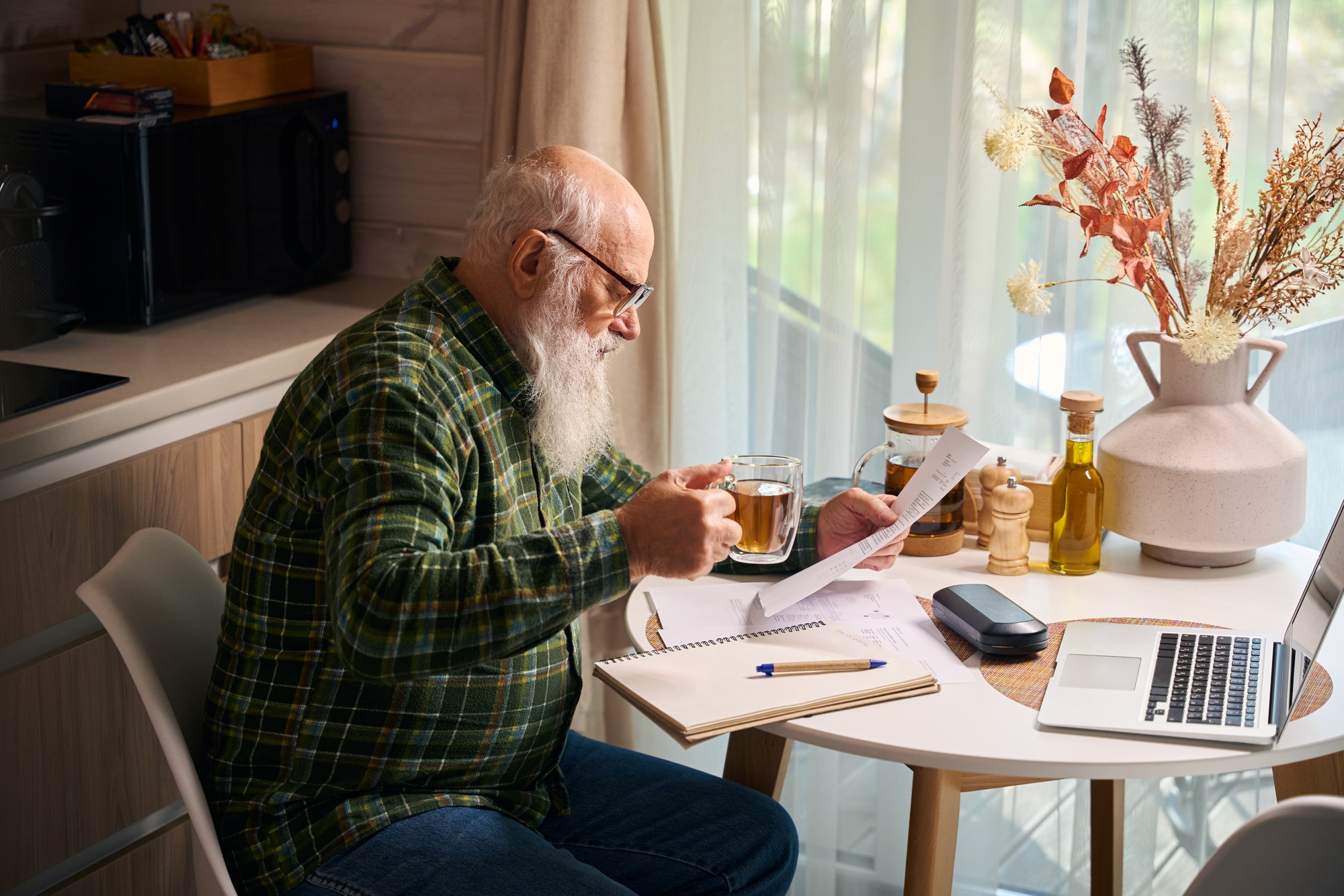 Elderly man works at the kitchen table on a laptop